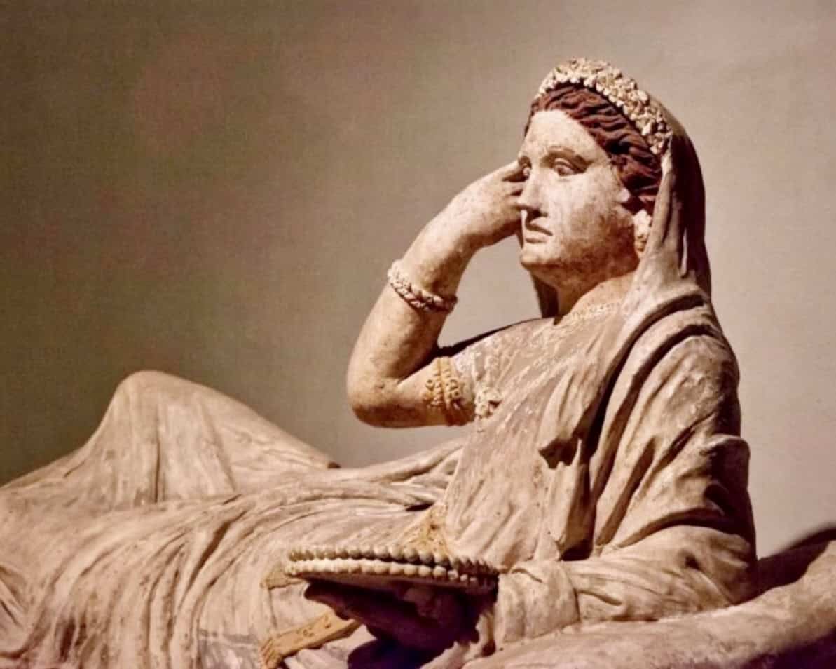 An Etruscan terracotta sarcophagus lid depicting one Larthia Seianti. 2nd century BCE. The woman has her right hand up to her face and is lying recumbant looking to her left.