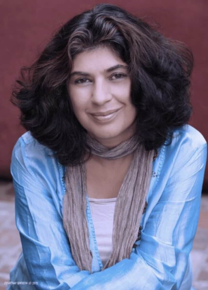 Mitra Rahbar smiles for the camera. She has shoulder-length cark hair and is wearing a light blue satin blouse over a white top. She's wearing a taupe-colored scarf.