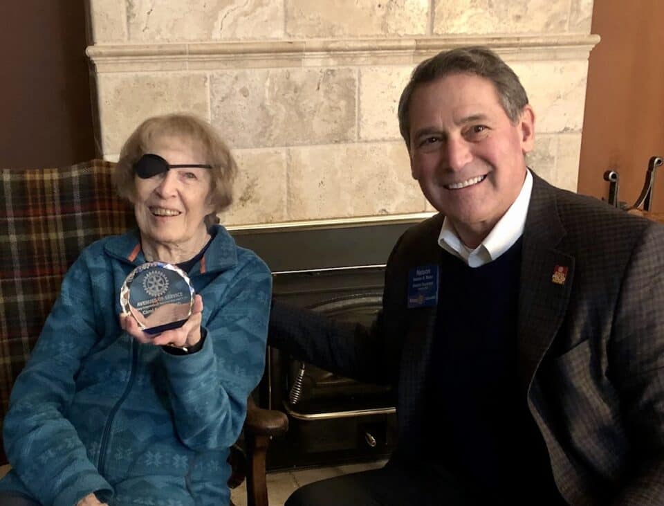 Carol Fellows holds an embossed glass award. District Governor Nelson Maler smiles next to her.