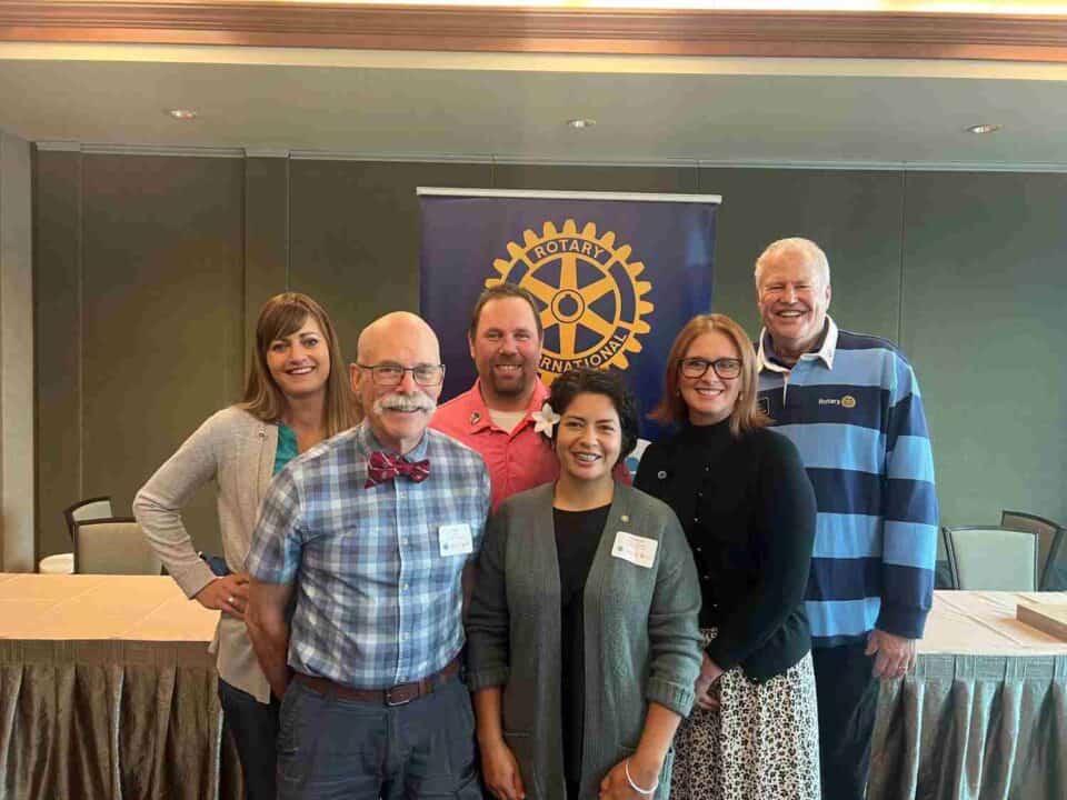 RLI presenters stand in front of a table and a banner featuring the Rotary logo